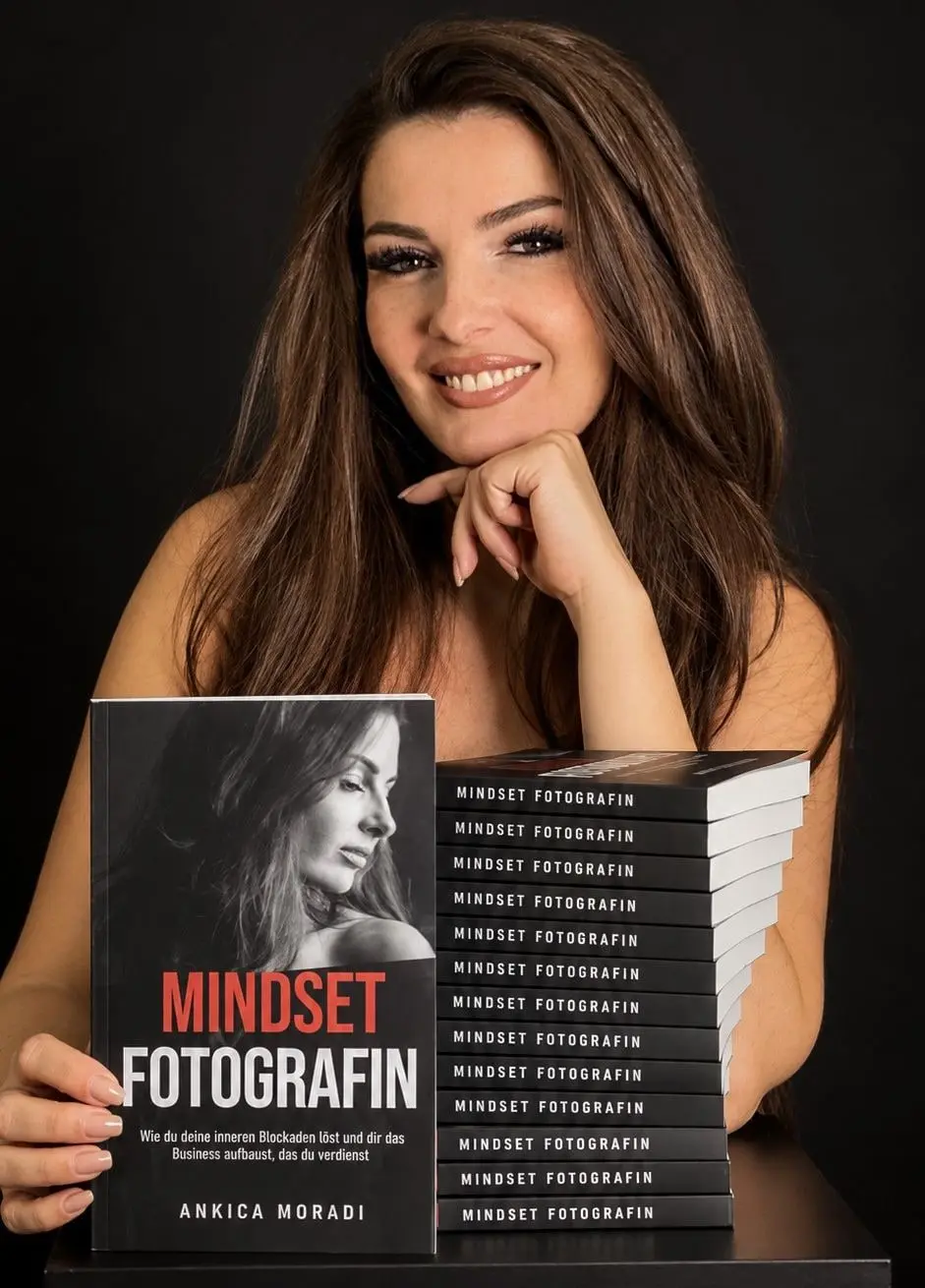 Ankica Moradi lächelt und hält ihr Buch „Mindset Fotografin“, daneben ein Stapel weiterer Exemplare.